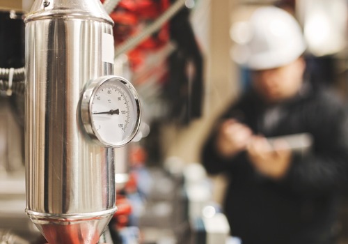 A closeup of a gauge as a technician performs a Boiler Inspection in IL in the background